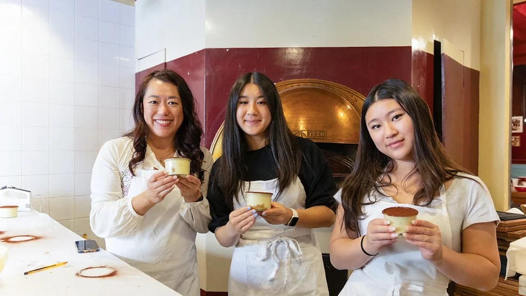 Participants holding tiramisu in a Rome cooking class kitchen.