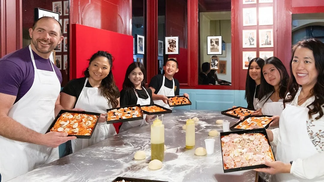 Participants in a Rome kitchen cooking class holding trays of prepared pizza dough.