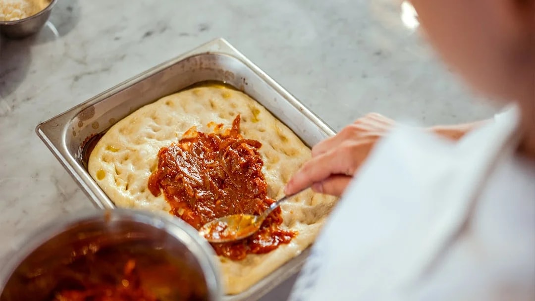 Spreading tomato sauce on pizza dough during cooking class in Palermo.
