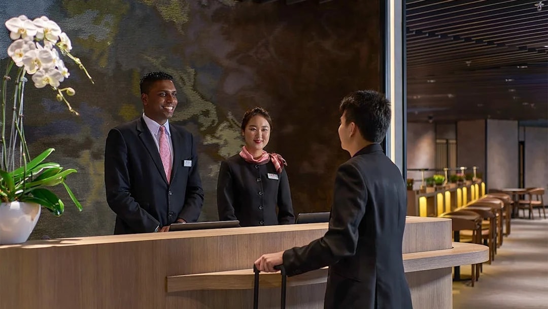 Reception desk at Plaza Premium First, Satellite Terminal, with staff assisting a traveler.