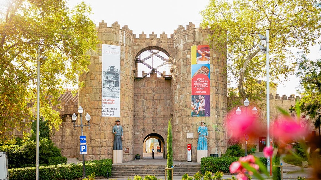Entrance to Poble Espanyol in Barcelona with stone archway and colorful banners.