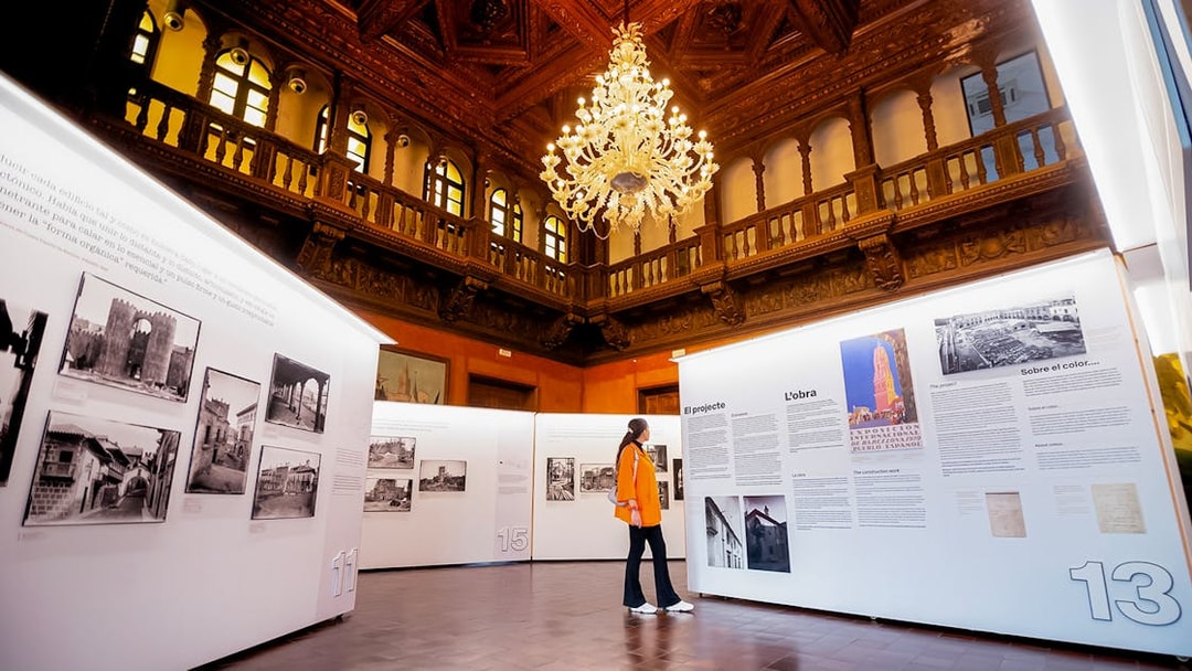 Visitor exploring an exhibition inside Poble Espanyol, Barcelona, with ornate ceiling and chandelier.