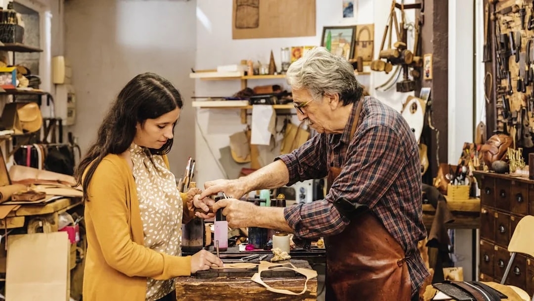Craftsman demonstrating leatherwork to a tourist at Poble Espanyol workshop.