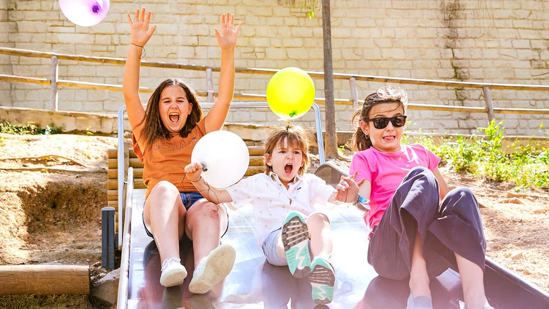 Children enjoying a slide at Poble Espanyol, Barcelona, holding colorful balloons.