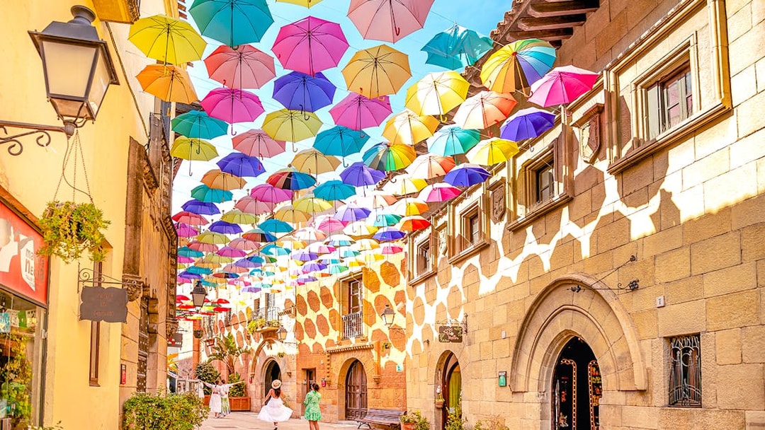 Tourists walking under colorful umbrellas in Poble Espanyol, Barcelona.