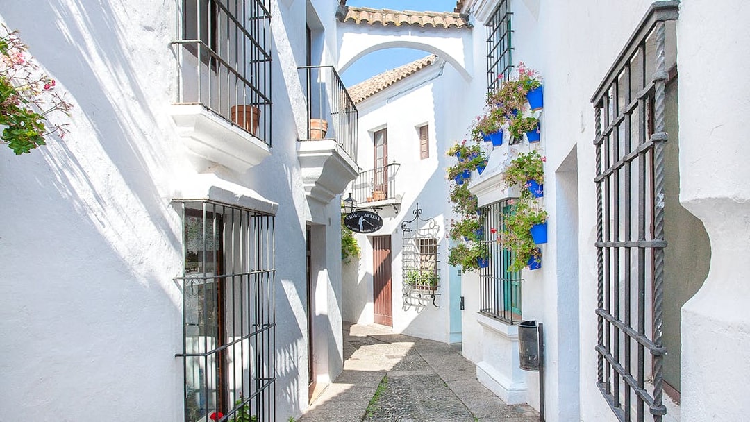 Narrow street with white buildings and flower pots in Poble Espanyol, Barcelona.