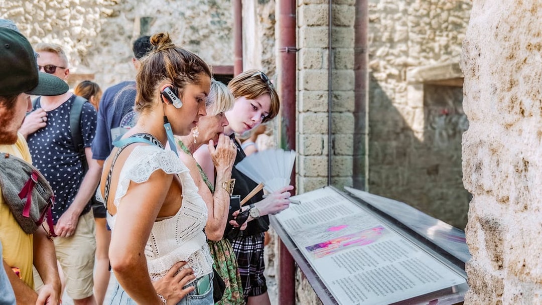 Visitors reading informational displays on a guided tour in Pompeii.