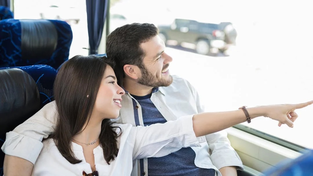 Couple smiling and pointing out the window on a bus tour.