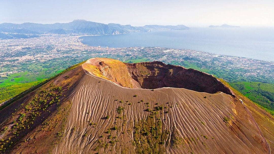 Aerial view of Mount Vesuvius crater with Naples and coastline in the background.