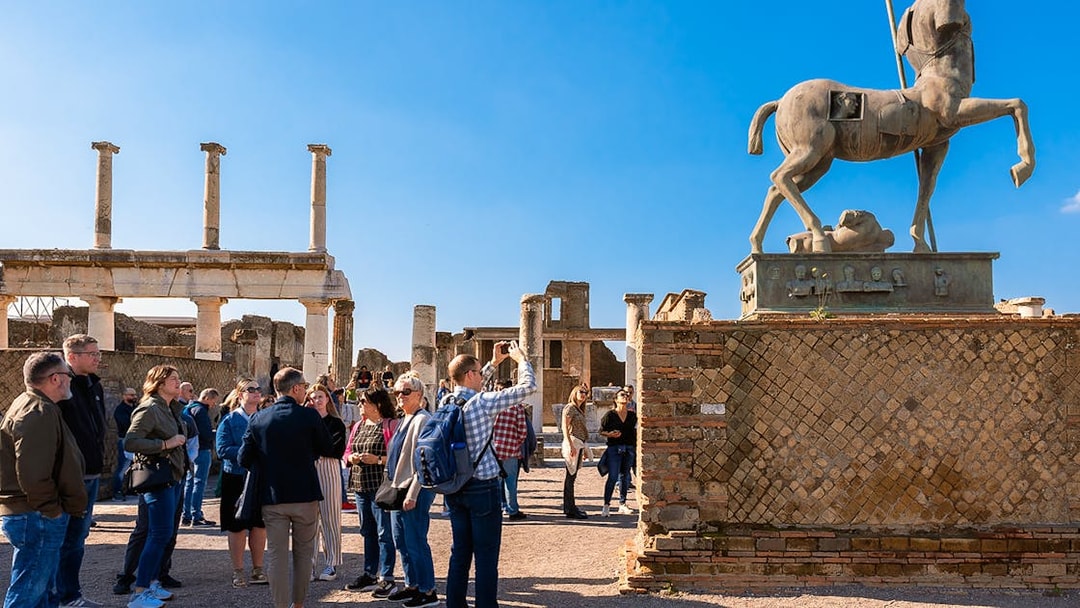 Visitors with a guide exploring the ancient ruins of Pompeii with a centaur statue in view.