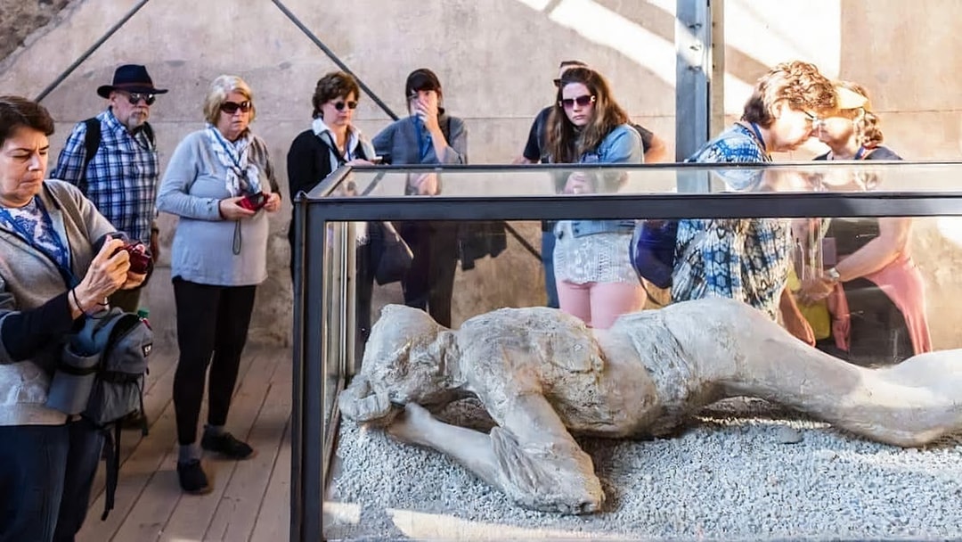 Visitors observing a plaster cast of a volcano victim in Pompeii.