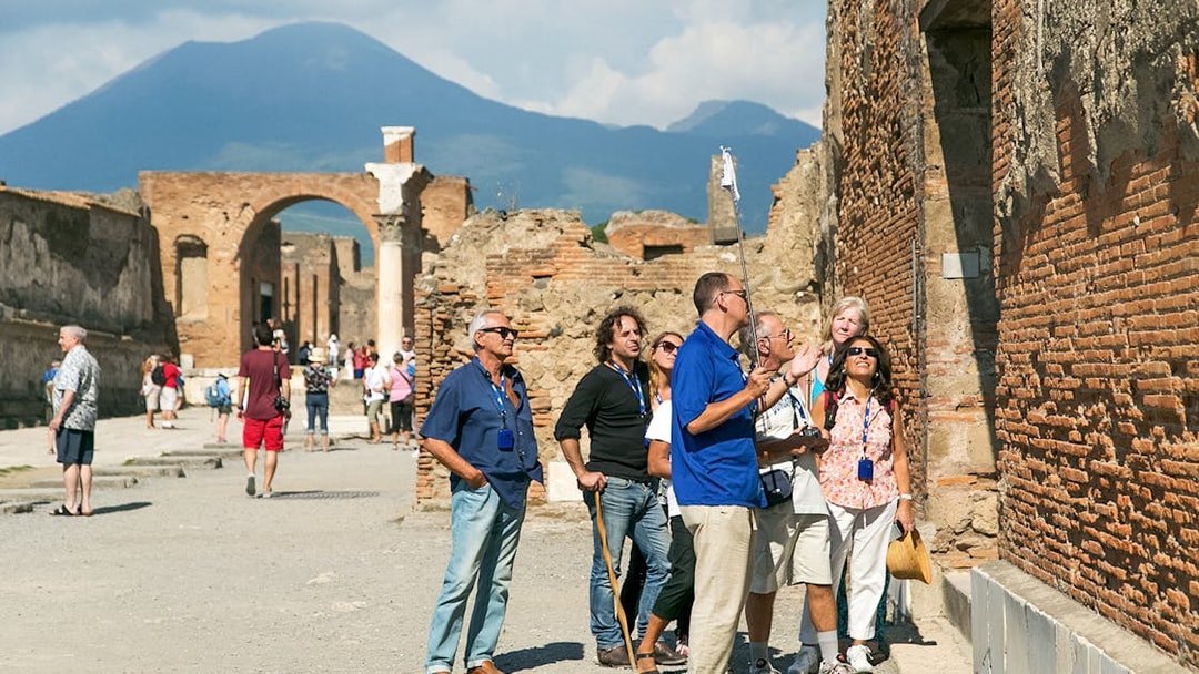 Guide explaining Pompeii ruins to tourists with Mount Vesuvius in the background.