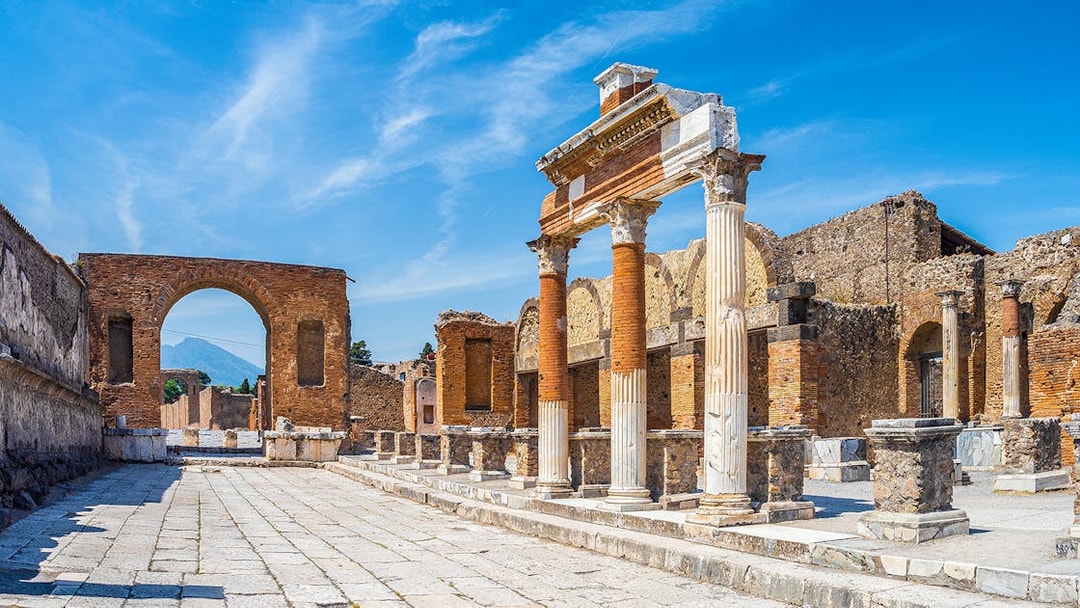 Ancient ruins of Pompeii with stone columns and archway under a clear blue sky.