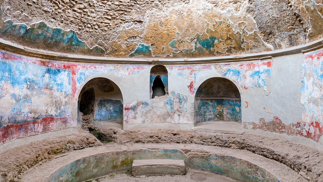 Pompeii Baths ancient frescoes and stone seating in circular room.