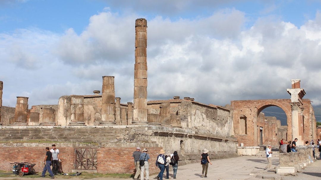Panoramic view of Pompeii ruins with visitors exploring ancient columns and archway.