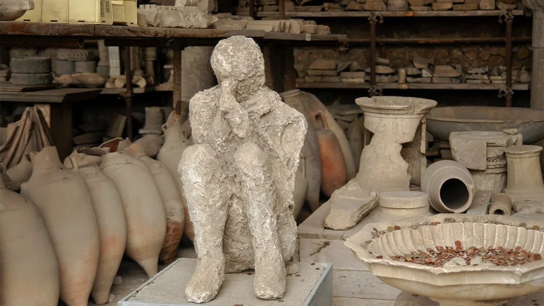Pompeii plaster cast of a victim with ancient artifacts in the background.