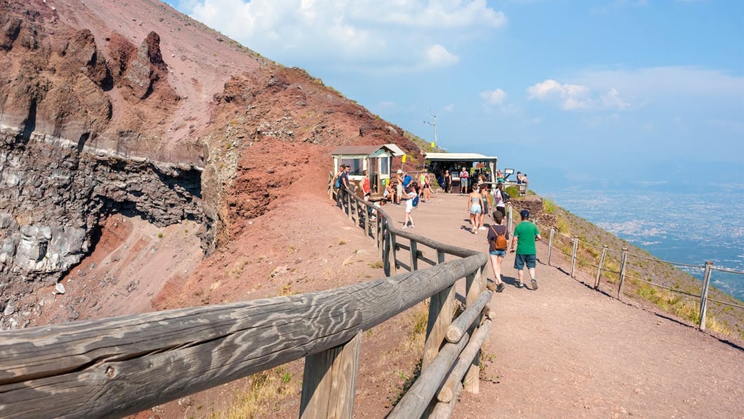 Visitors walking along the path on Mount Vesuvius with a view of the crater and Naples in the distance.