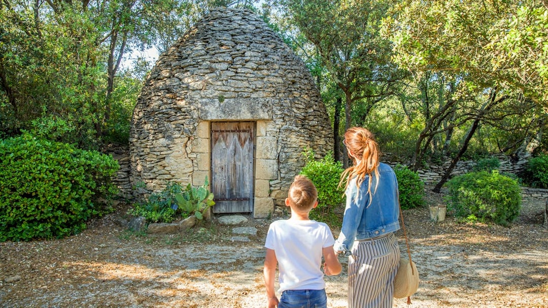 Visitors exploring a stone hut near Pont du Gard, surrounded by lush greenery.