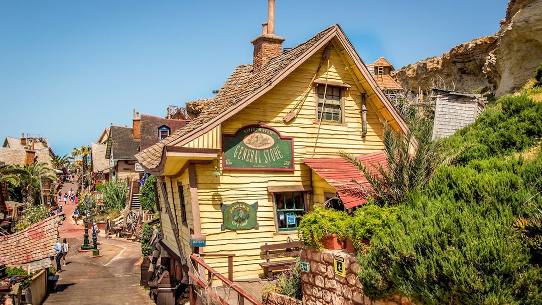 General store facade in Popeye Village, Malta, with colorful wooden buildings and greenery.