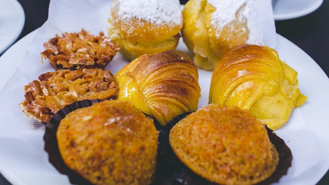 Portuguese pastries including almond tarts and sugar-dusted rolls on a plate.