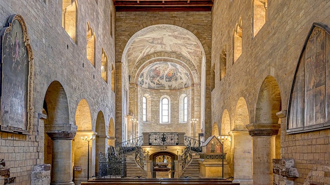 Interior of Basilica of St George with arched stone walls and ornate frescoed ceiling.