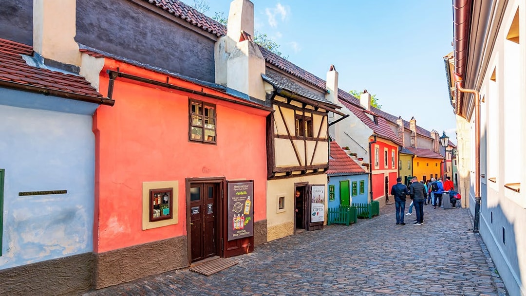 Colorful historic houses on Golden Lane, Prague, with tourists walking along the cobblestone street.