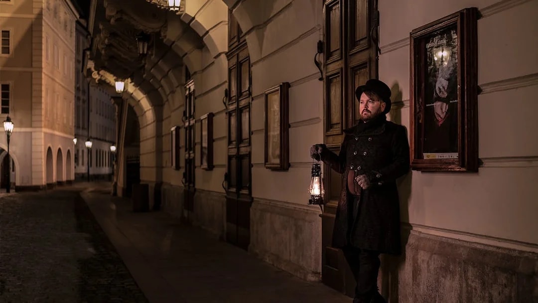 Guide holding lantern in Prague's Old Town during night-time ghost tour.