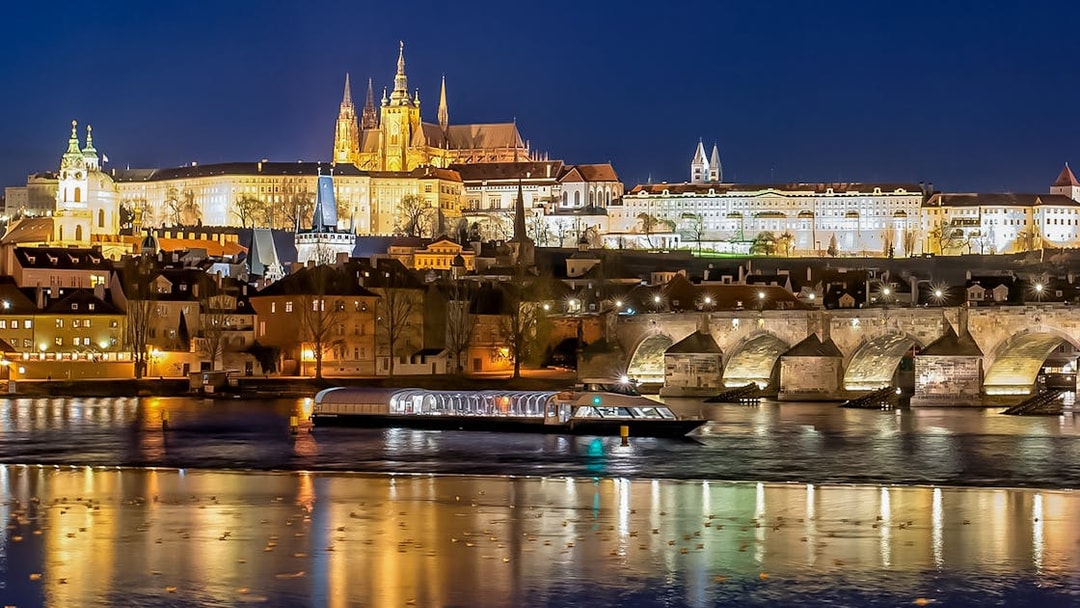 Open-top glass boat on Vltava River with Prague Castle and Charles Bridge illuminated at night.