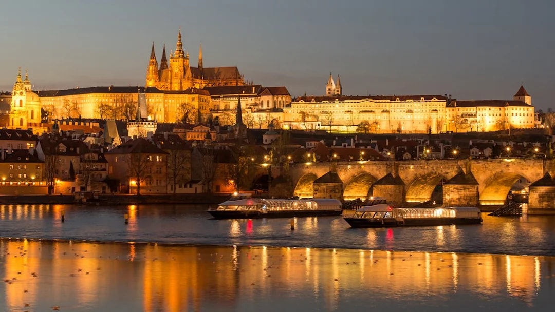 Open-top glass boat on Vltava River with Prague Castle illuminated at night.