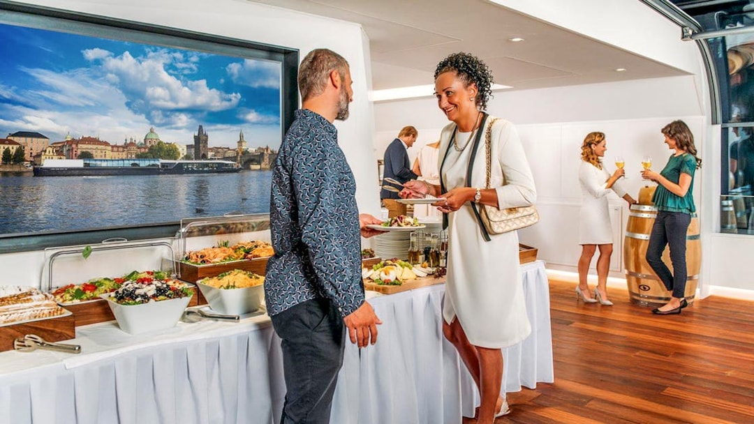 Guests enjoying a buffet on a Prague dinner cruise with a view of the Vltava River.
