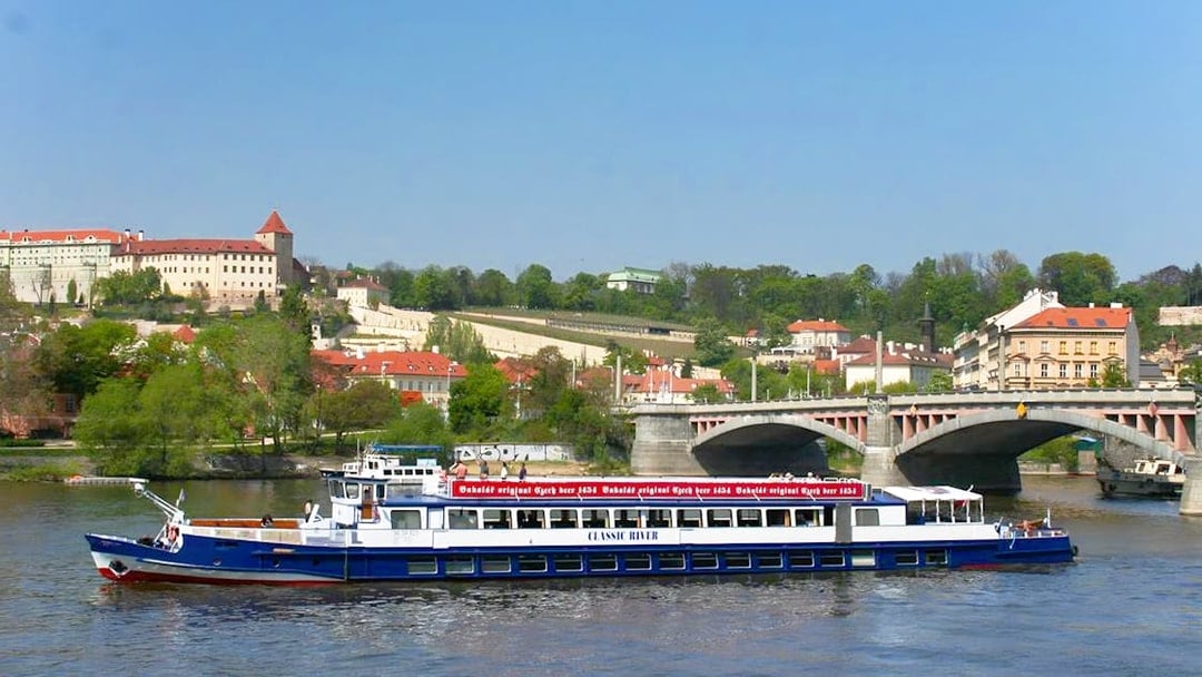 River cruise boat on Vltava River with Prague Castle in the background.