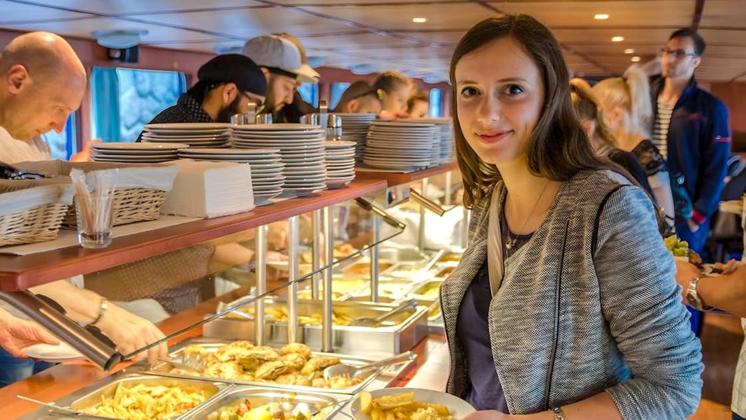 Guests serving food at buffet on evening dinner cruise with live music.