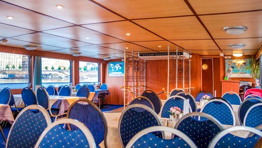 Interior of a Prague sightseeing boat with dining tables and river view.