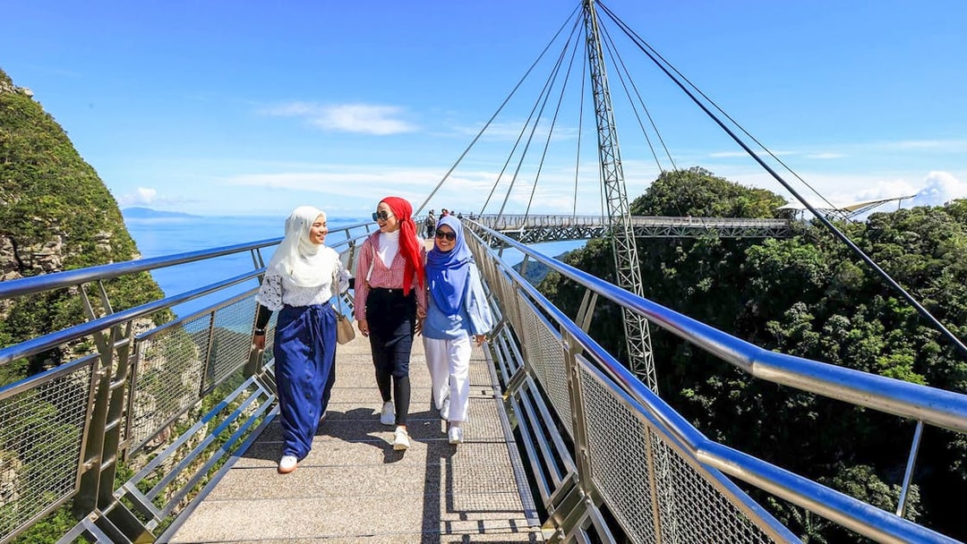 Women walking on Langkawi Skybridge with scenic views of mountains and ocean.