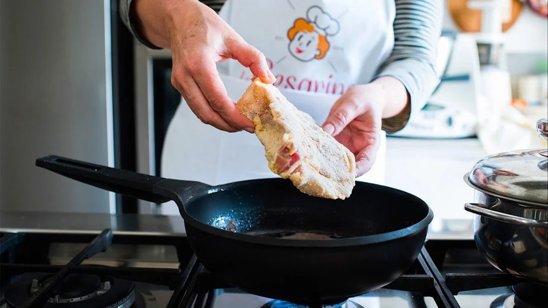 Person preparing breaded cutlet in a private cooking class in Milan kitchen.
