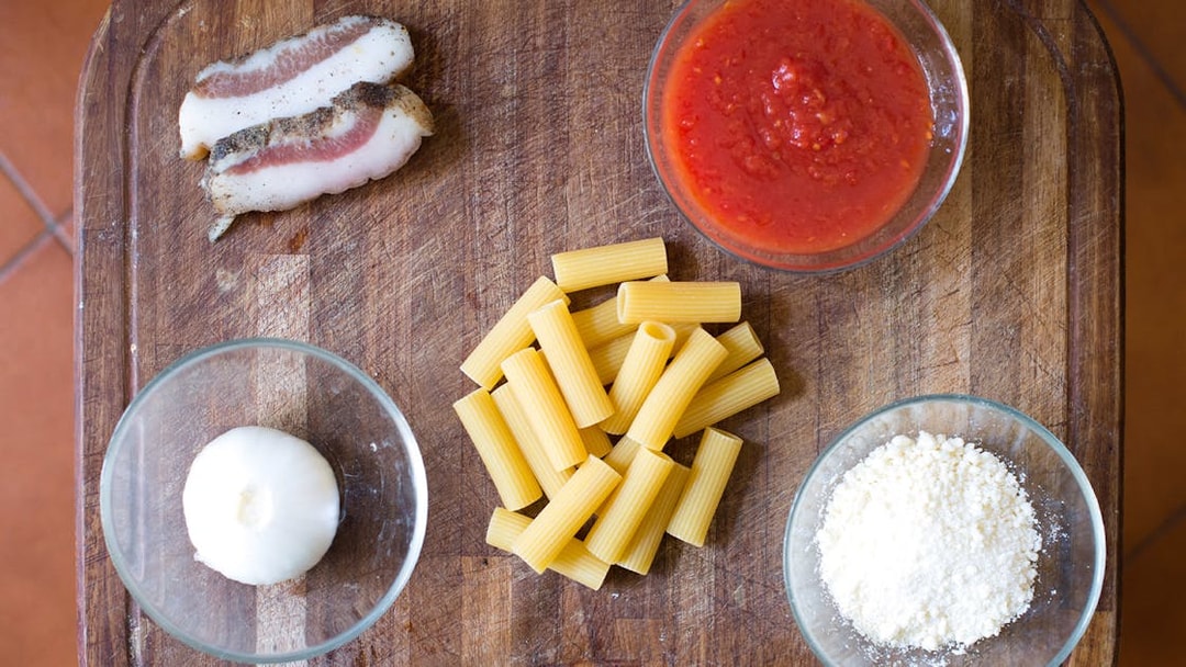 Pasta ingredients for a private cooking class in Rome, including rigatoni, pancetta, tomato sauce, onion, and cheese.