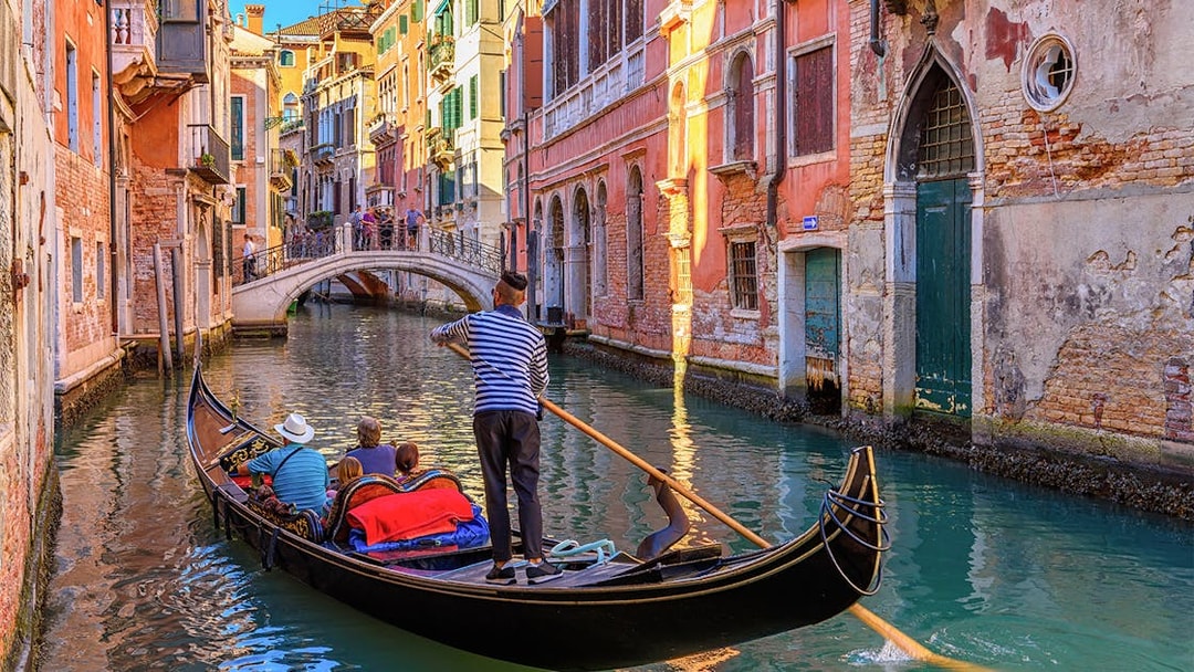 Gondola navigating a narrow canal in Venice with colorful buildings and a small bridge.