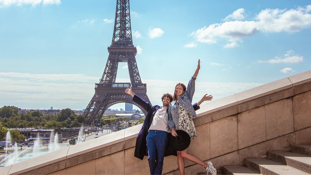 Couple posing joyfully in front of the Eiffel Tower during a private photoshoot in Paris.
