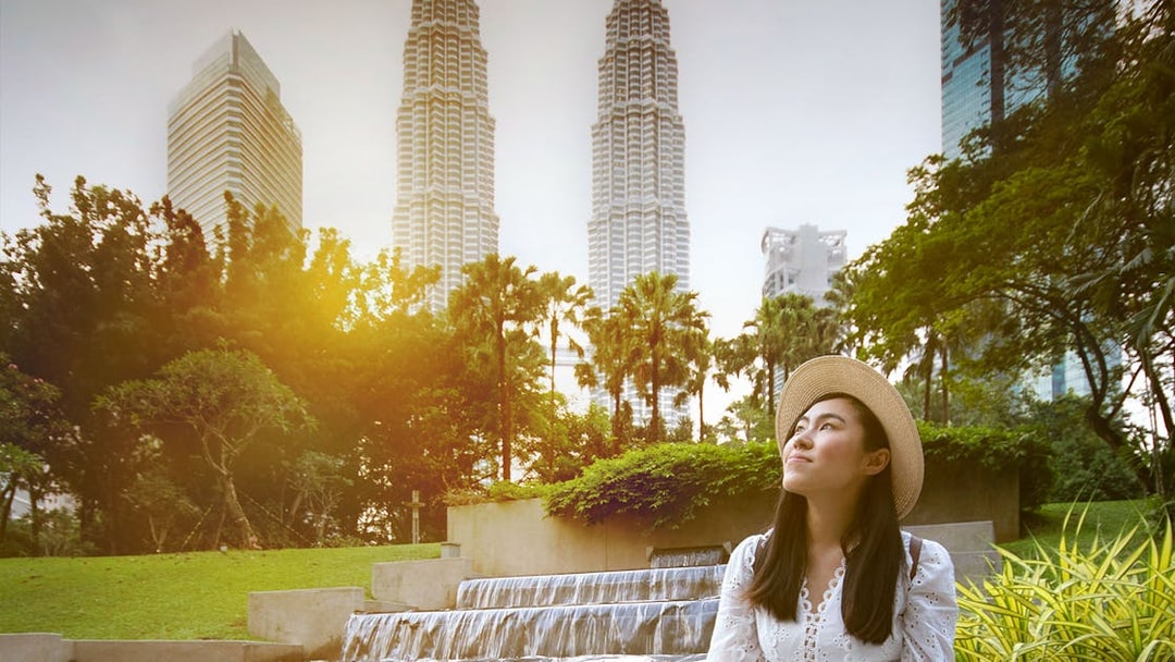 Woman in a hat posing in front of Kuala Lumpur's Petronas Towers.