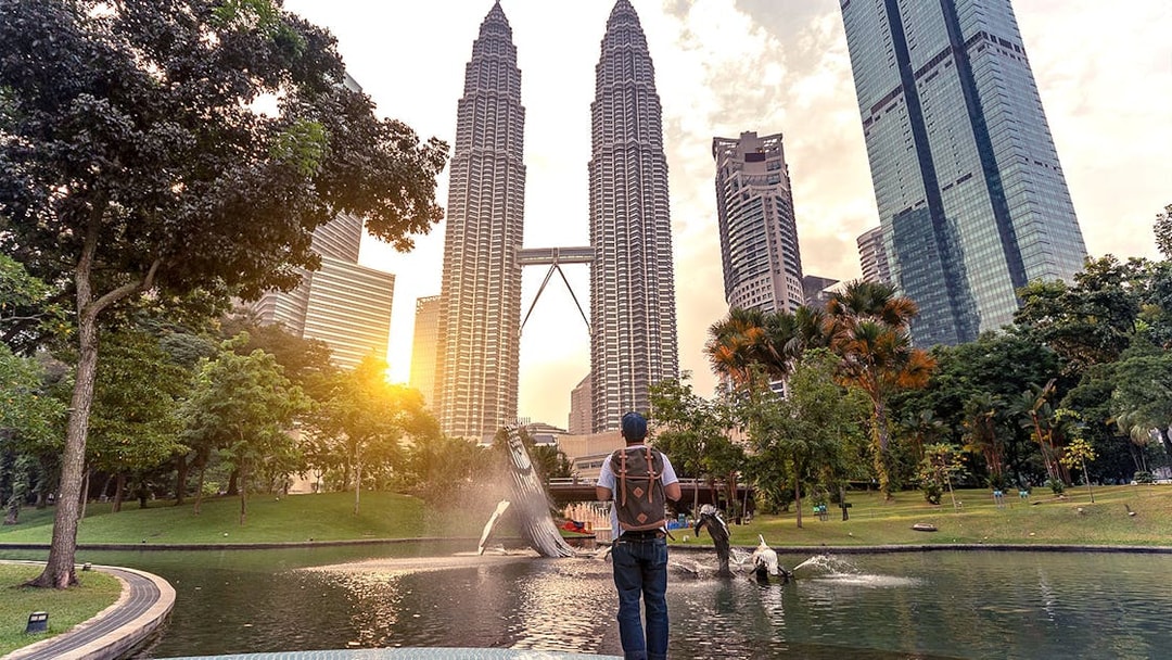 Traveler at Petronas Towers, Kuala Lumpur, with sunset and fountain in the foreground.
