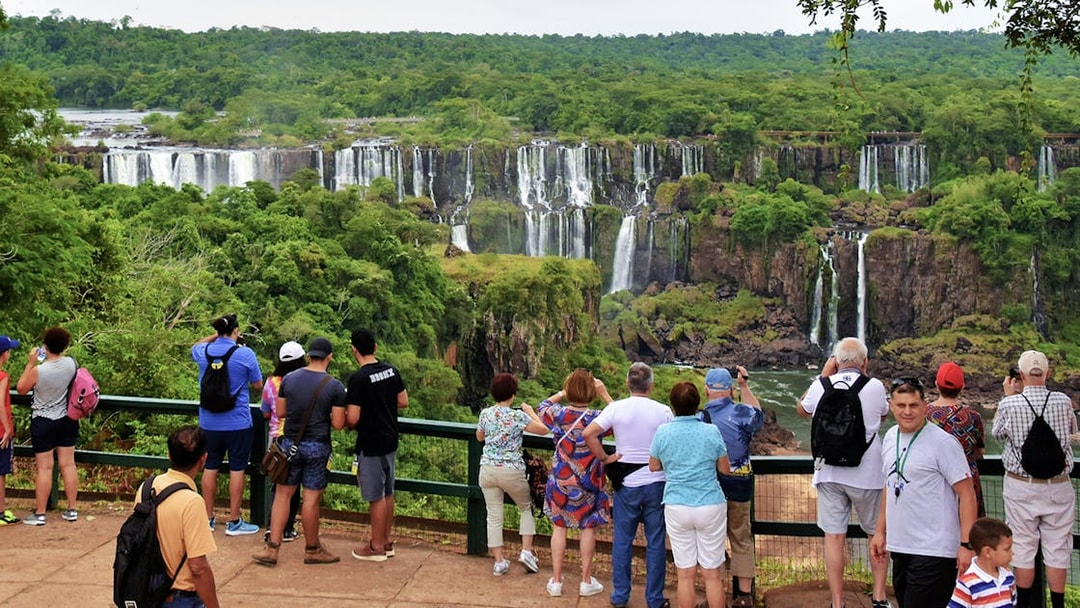 Visitors viewing Iguazu Falls from a lookout point surrounded by lush greenery.