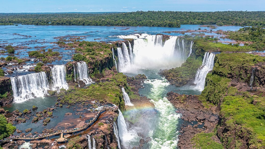 Aerial view of Iguazu Falls with a rainbow and lush greenery.