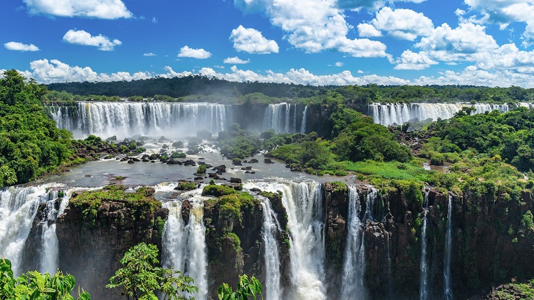 Iguazu Falls cascading over lush green cliffs under a blue sky.