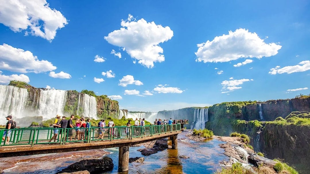 Visitors on a walkway at Iguazu Falls, Brazil, with cascading waterfalls in the background.