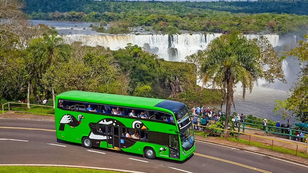 Green tour bus near Brazilian Falls with tourists viewing the waterfall.