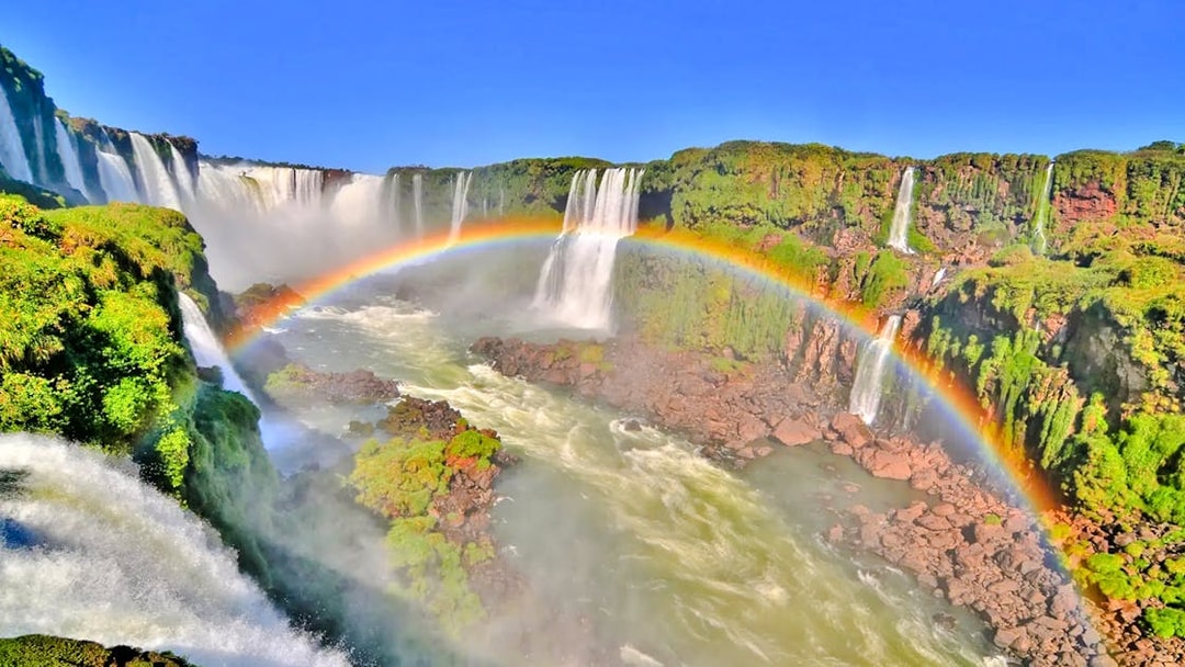 Waterfalls at Brazilian Falls with a rainbow arching over lush greenery.
