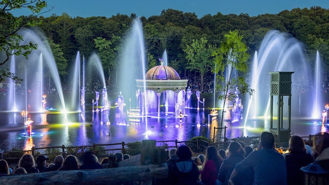 Nighttime fountain show at Puy du Fou with illuminated water jets and audience.
