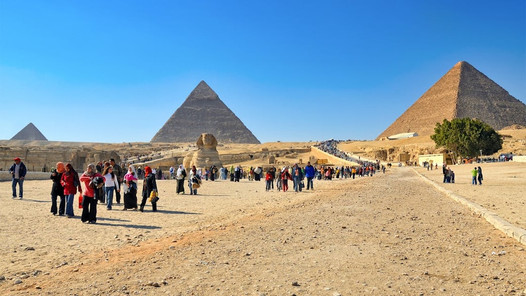 Tourists exploring the Pyramids of Giza and the Sphinx on a sunny day in Egypt.