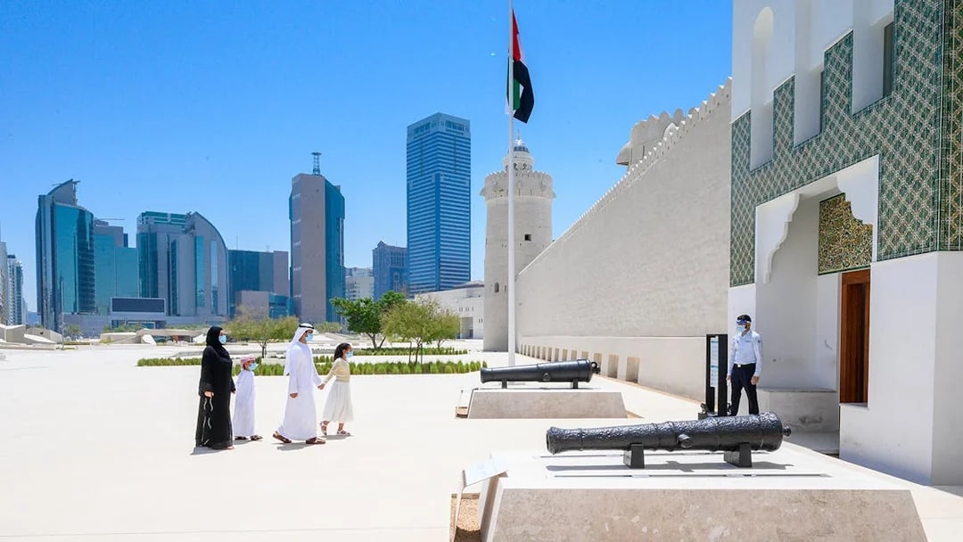 Qasr Al Hosn exterior with visitors and historic cannons, Abu Dhabi skyline in background.