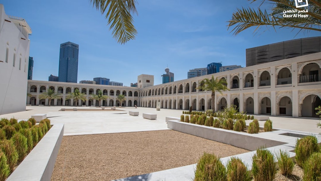 Qasr Al Hosn courtyard with palm trees and modern city skyline in Abu Dhabi.